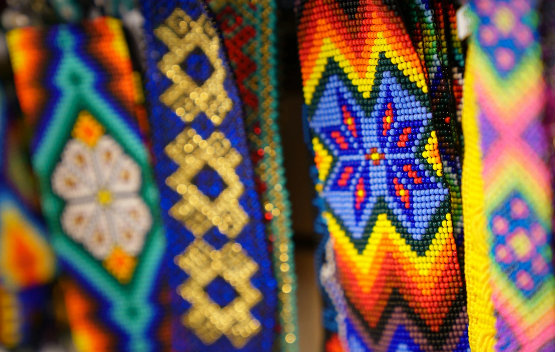 Tissage de perle avec différent motif et de couleurs ceux de derrière son un peu flou et le premier et une croix bleu avec un dégrader, jaune, orange, rouge...