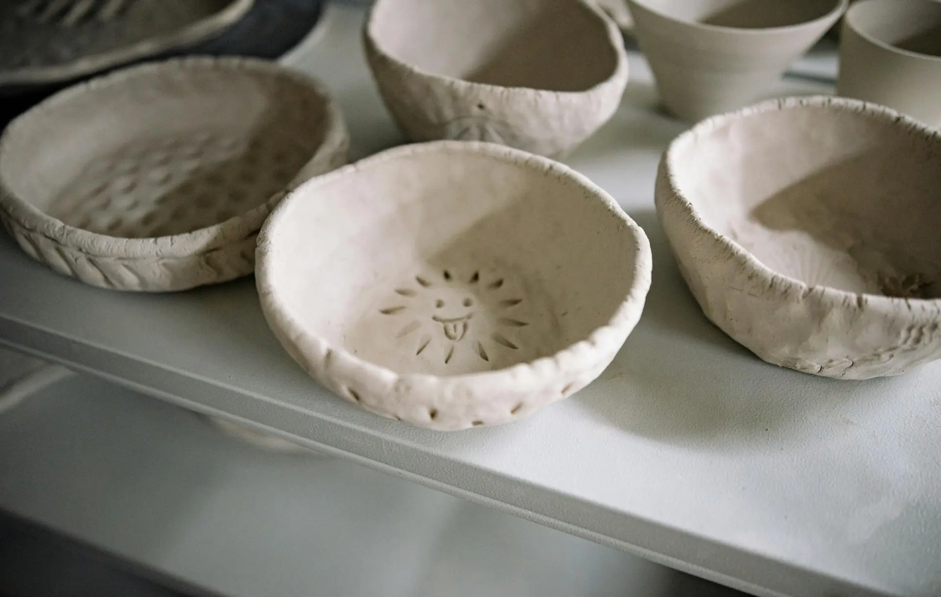 plusieurs petit bol en argile non plein, brute avec un bol avec un visage qui ressemble à un soleil qui tire la langue